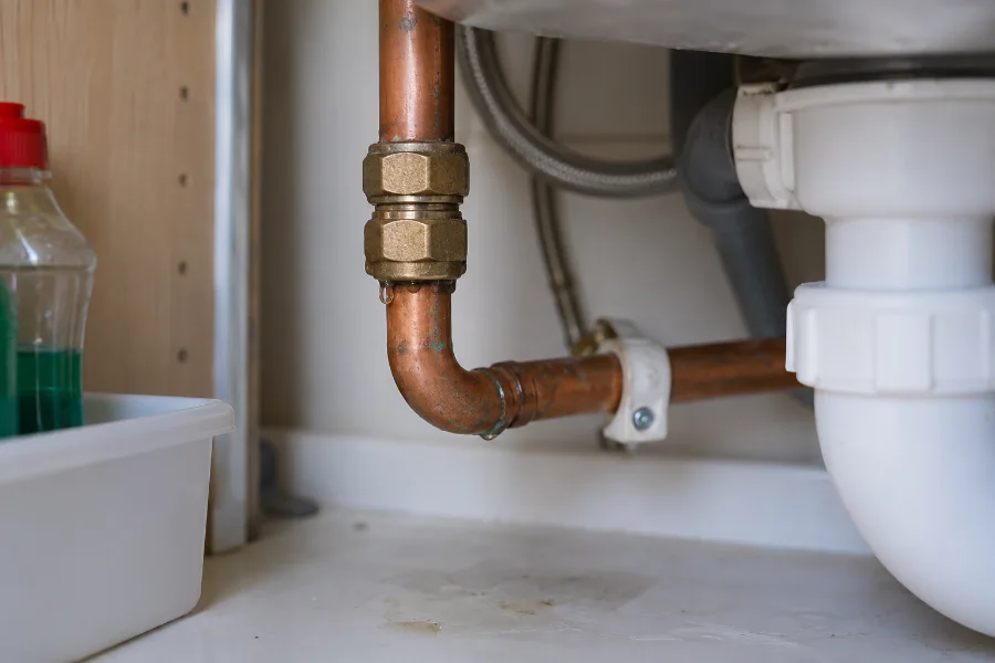 Water droplets on a copper pipe joint beneath a kitchen sink